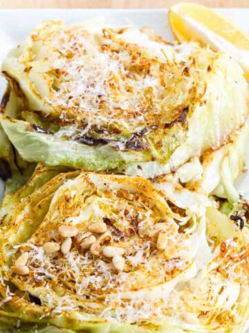 Cabbage steaks on a white rectangle platter garnished with parmesan cheese and toasted pine nuts.