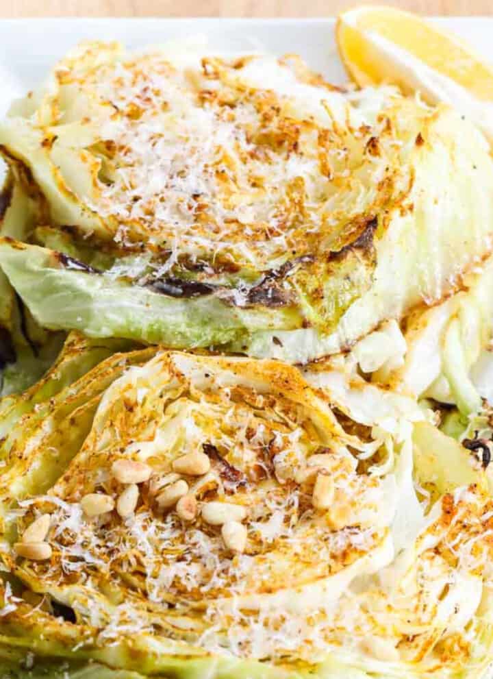 Cabbage steaks on a white rectangle platter garnished with parmesan cheese and toasted pine nuts.