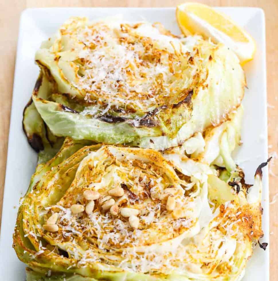 Cabbage steaks on a white rectangle platter garnished with parmesan cheese and toasted pine nuts.