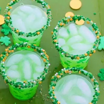 Four glasses of green cocktails for St. Patrick's day on a green tray with gold coins.