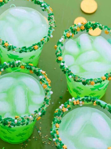 Four glasses of green cocktails for St. Patrick's day on a green tray with gold coins.