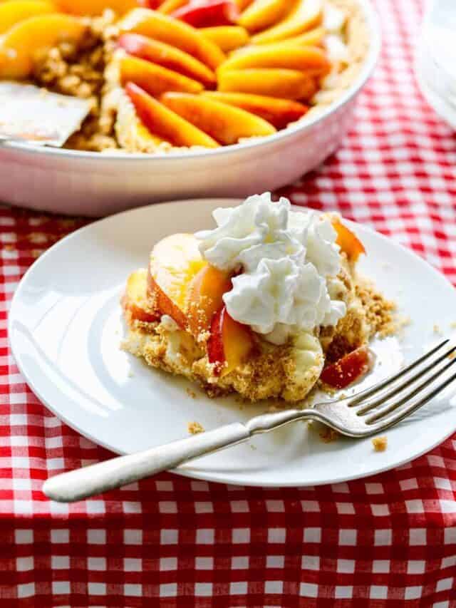A piece of peach ice box pie on a white plate with a silver fork on a red and white checked table cloth.