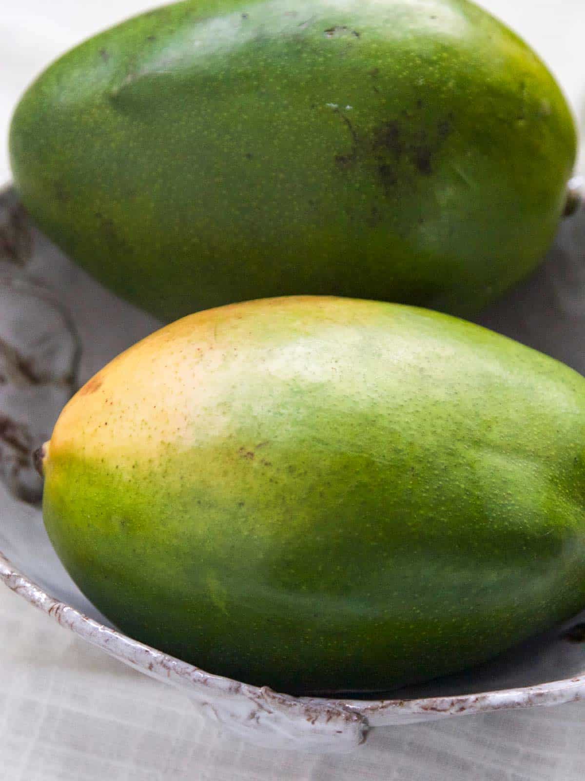 Two ripe mangos in a ceramic bowl to show how to cut a mango.