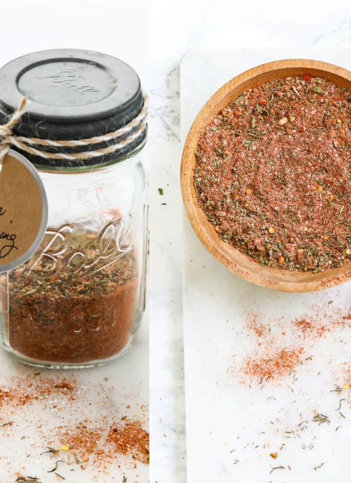A small glass mason jar filled with Cajun seasoning with a label and it in a wooden bowl.