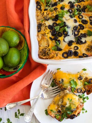 A white casserole dish with chicken enchilada casserole topped with black olives and lots of melted cheese.