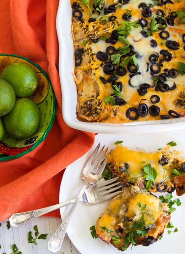 A white casserole dish with chicken enchilada casserole topped with black olives and lots of melted cheese.