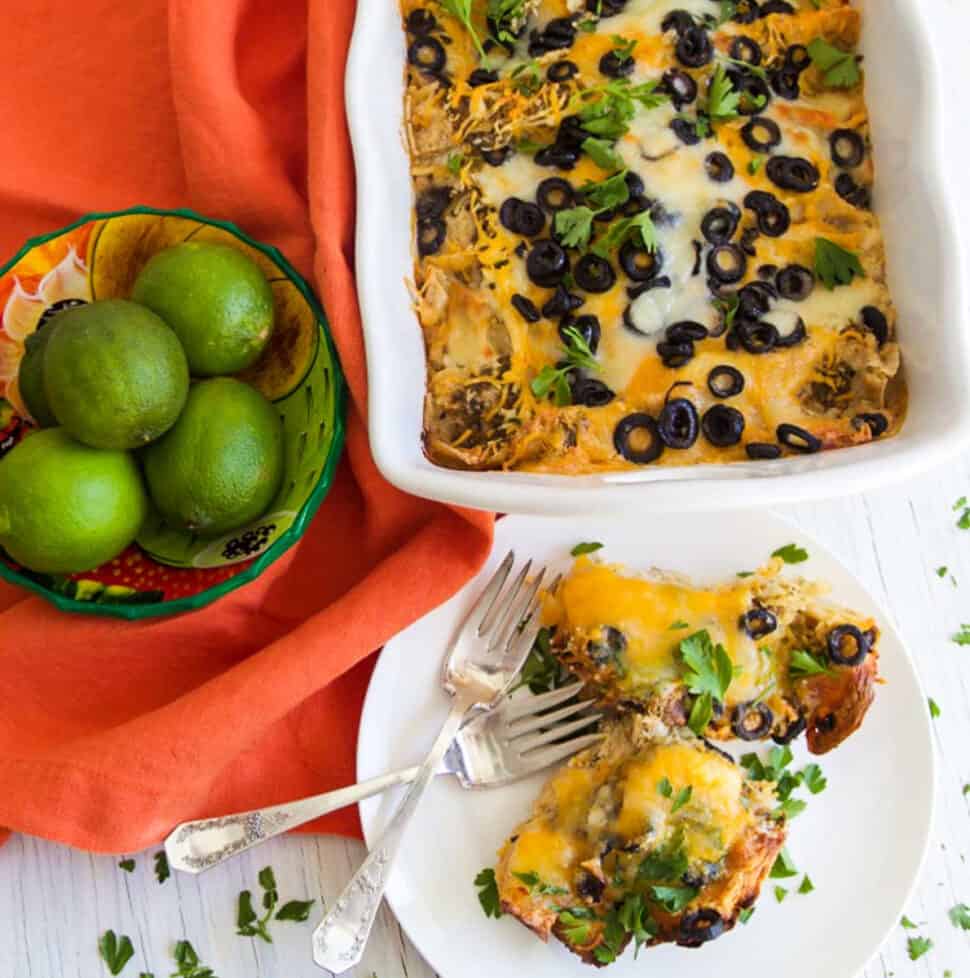 A white casserole dish with chicken enchilada casserole topped with black olives and lots of melted cheese.