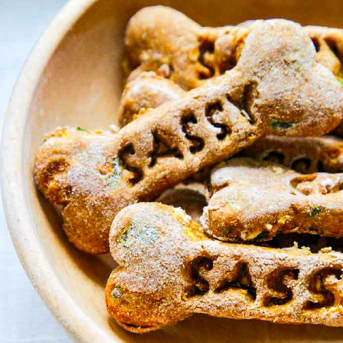 A wooden bowl with homemade dog treats and the name of the dog Sassy stamped in each of them in a pile.