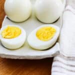 Whole hard boiled eggs on a ceramic tray and one sliced open revealing the yolk.