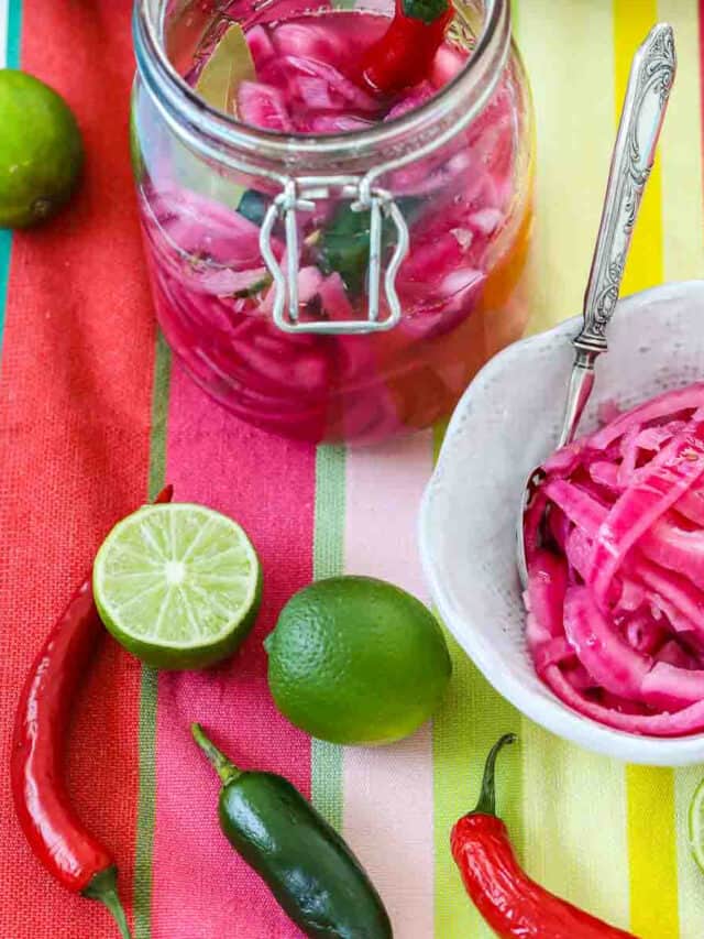 Mexican pickled red onions in a clamp jar and white bowl with chiles and limes on a colorful striped cloth.