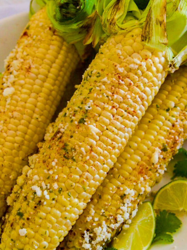 Several grilled elotes Mexican street corn on the cob sprinkled with Cotija cheese on a platter.