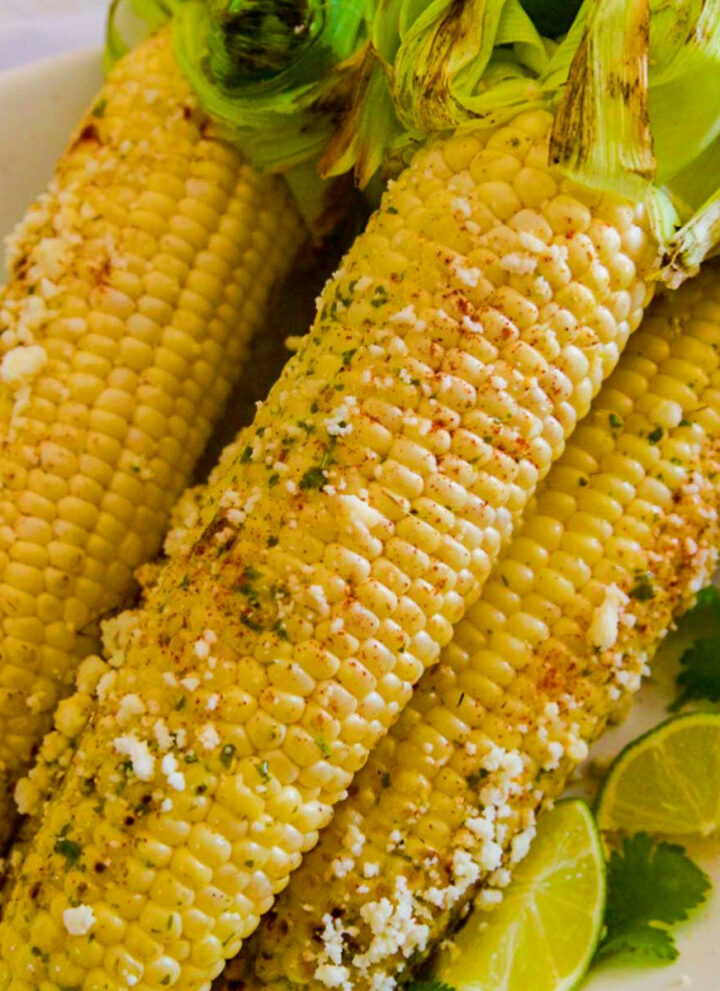 Several grilled elotes Mexican street corn on the cob sprinkled with Cotija cheese on a platter.