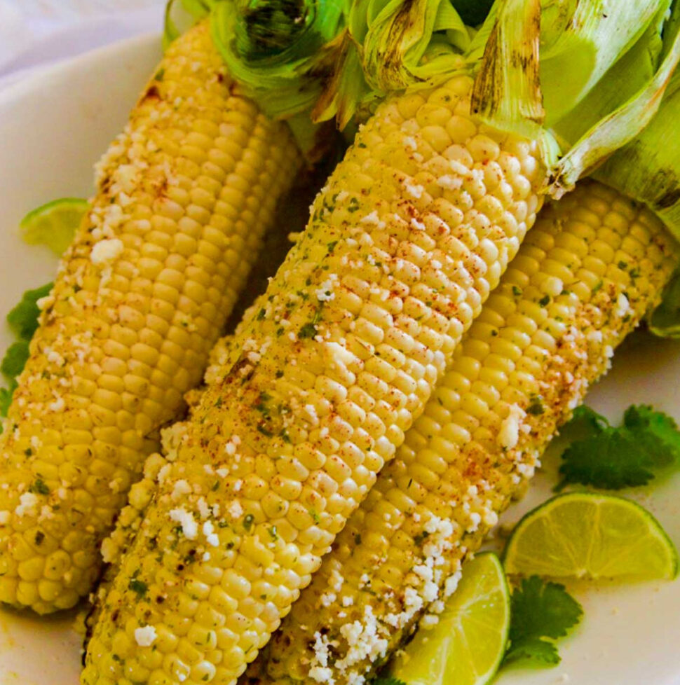 Several grilled elotes Mexican street corn on the cob sprinkled with Cotija cheese on a platter.