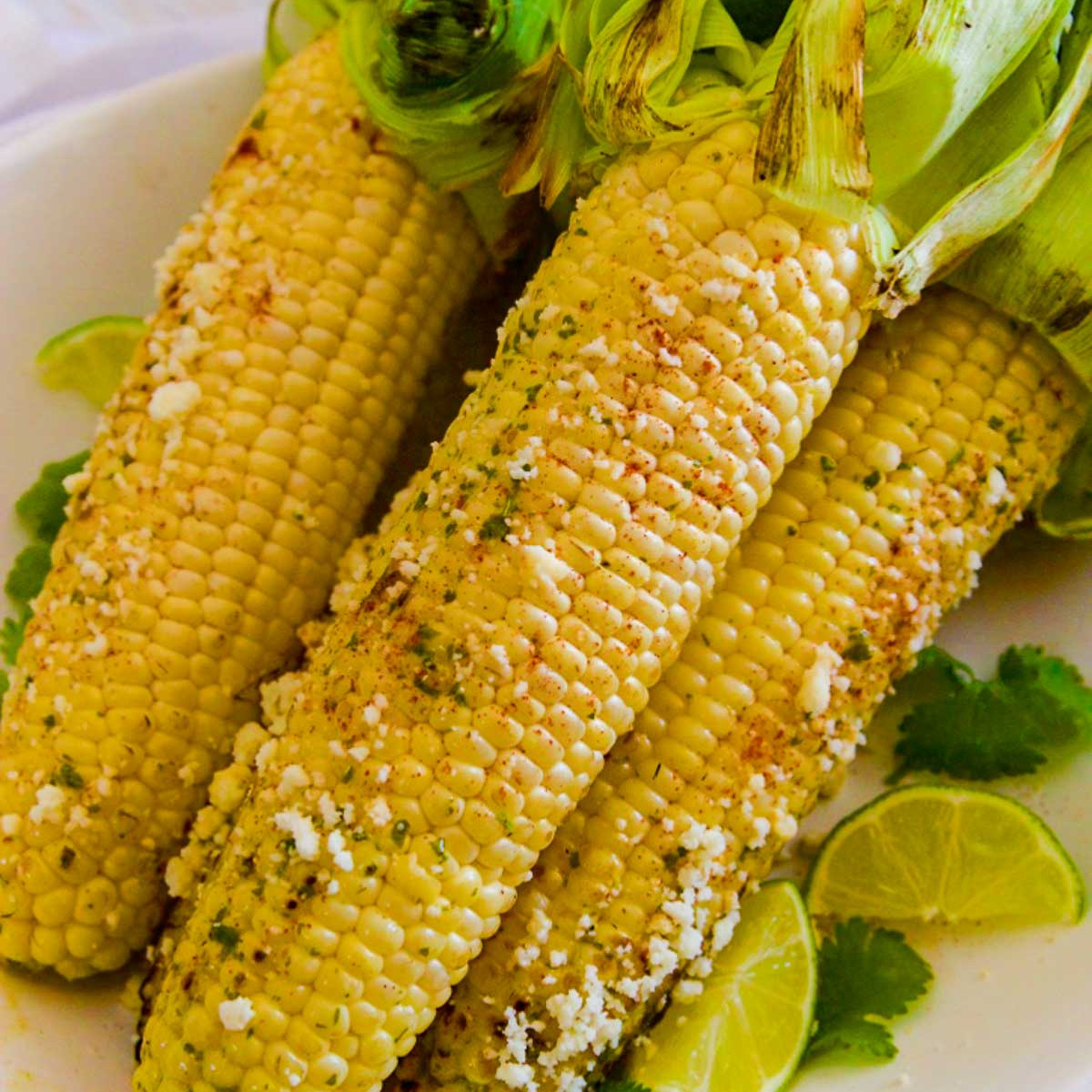 Several grilled elotes Mexican street corn on the cob sprinkled with Cotija cheese on a platter.