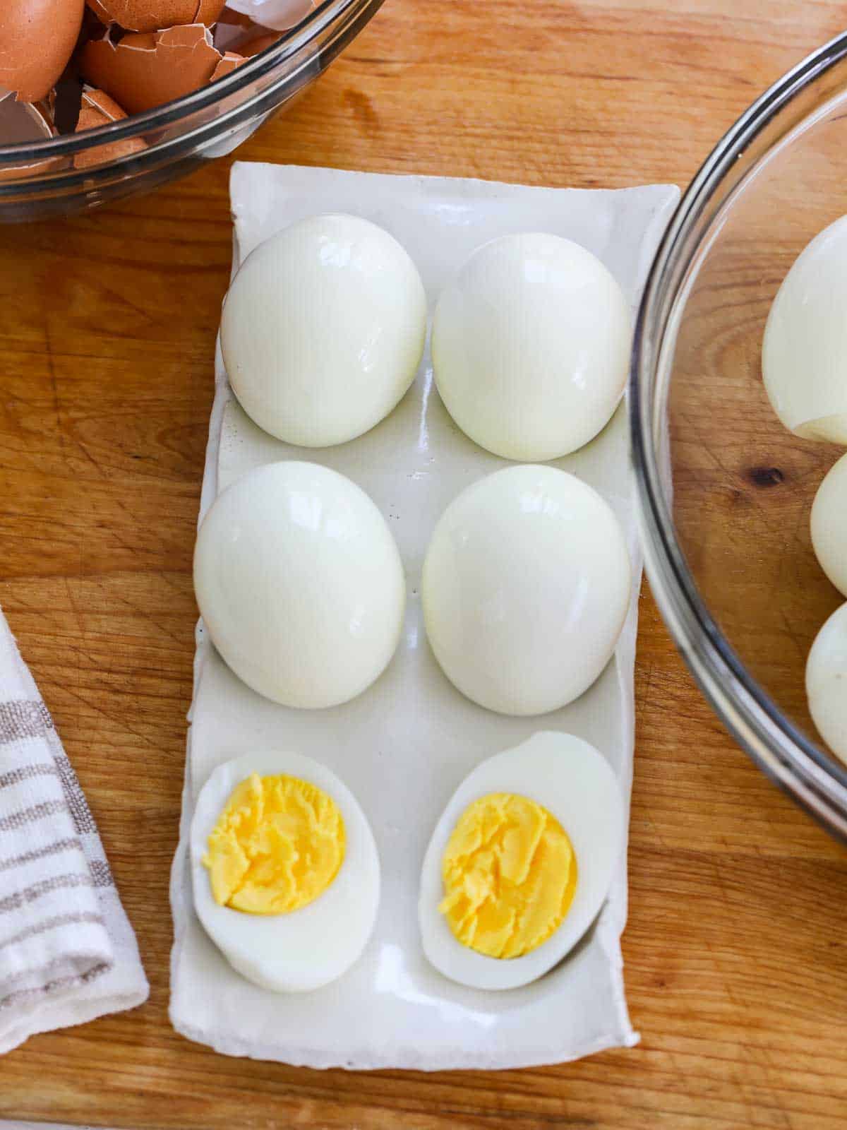 Looking down on a white ceramic egg dish with hard boiled eggs and one sliced open to reveal the yolk