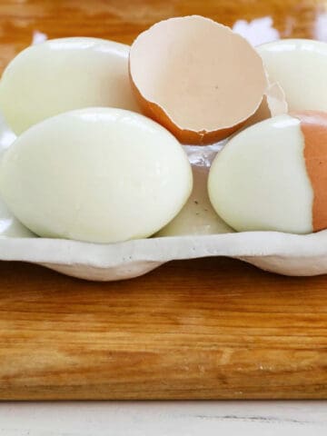 6 perfectly hard boiled eggs with a cracked half of an egg shelf on top.