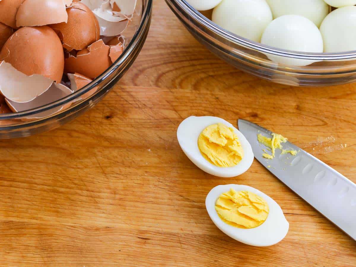 A hard boiled egg sliced open on a cutting board with egg shells nearby.