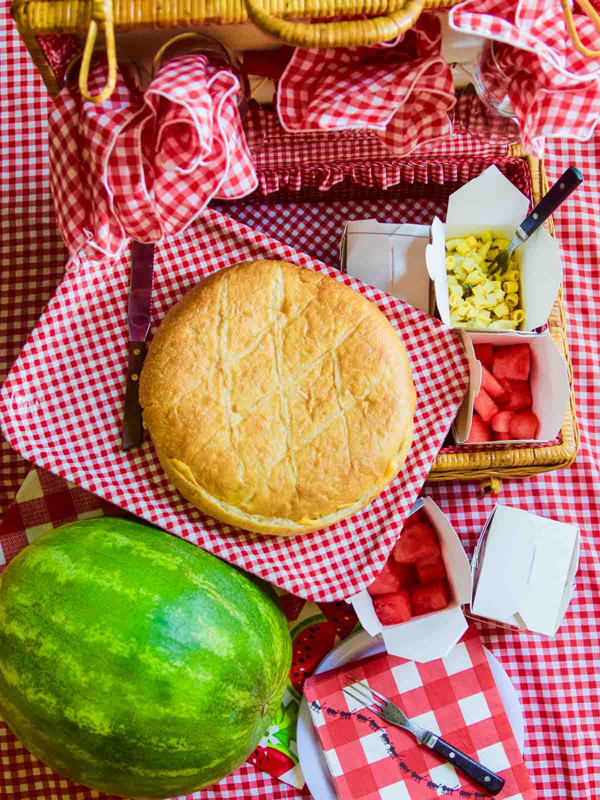 A round pressed picnic sandwich with a watermelon and red check picnic basket. 