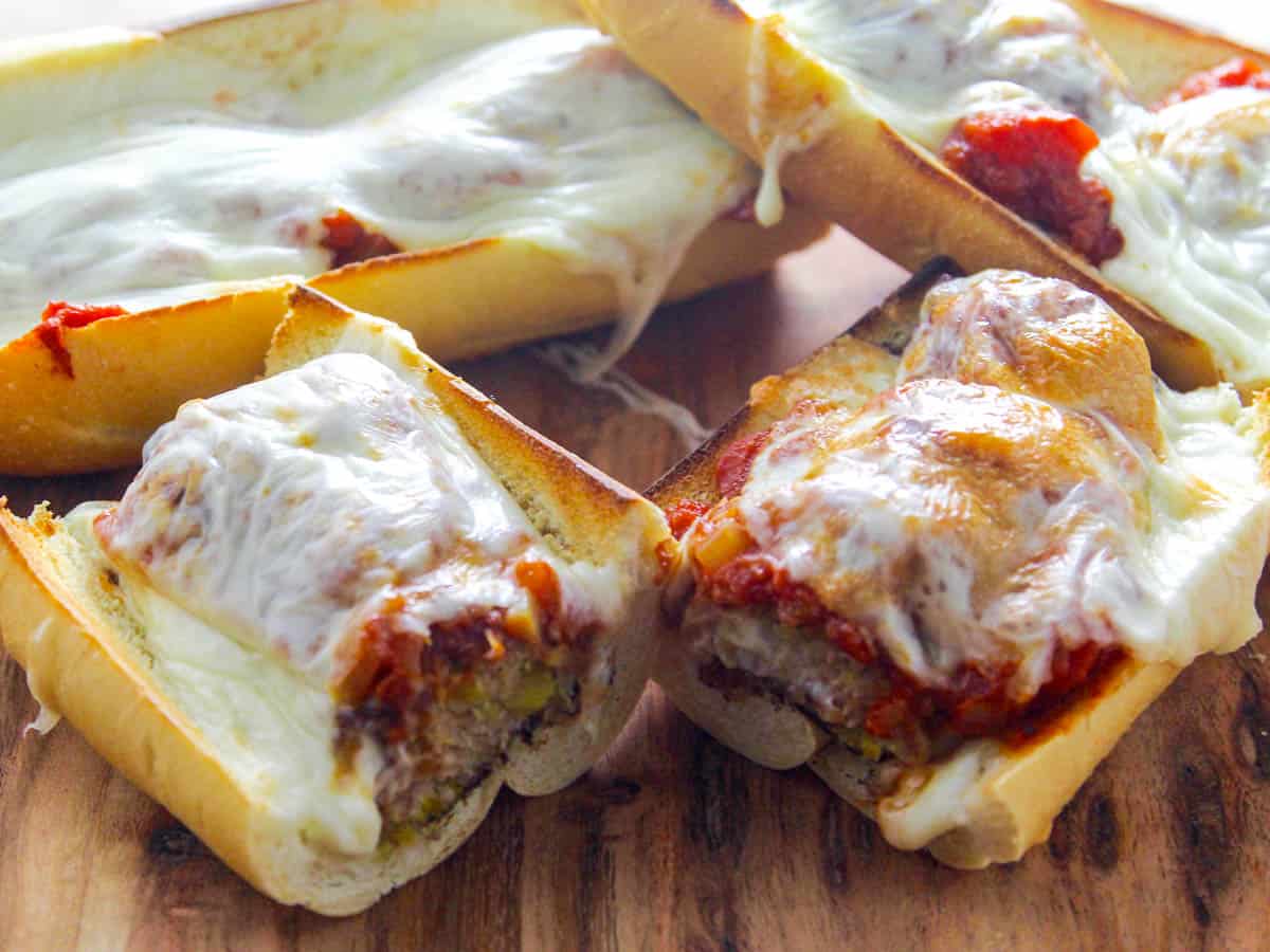 Sliced meatball sub sandwiches on a board covered in melted mozzarella cheese.