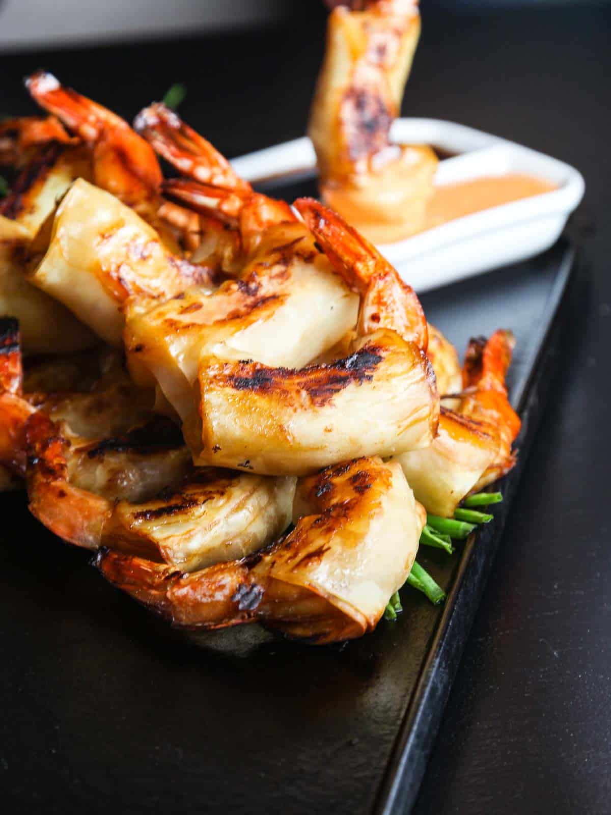 A pile of cooked spicy Chinese firecracker shrimp with sauces in background.