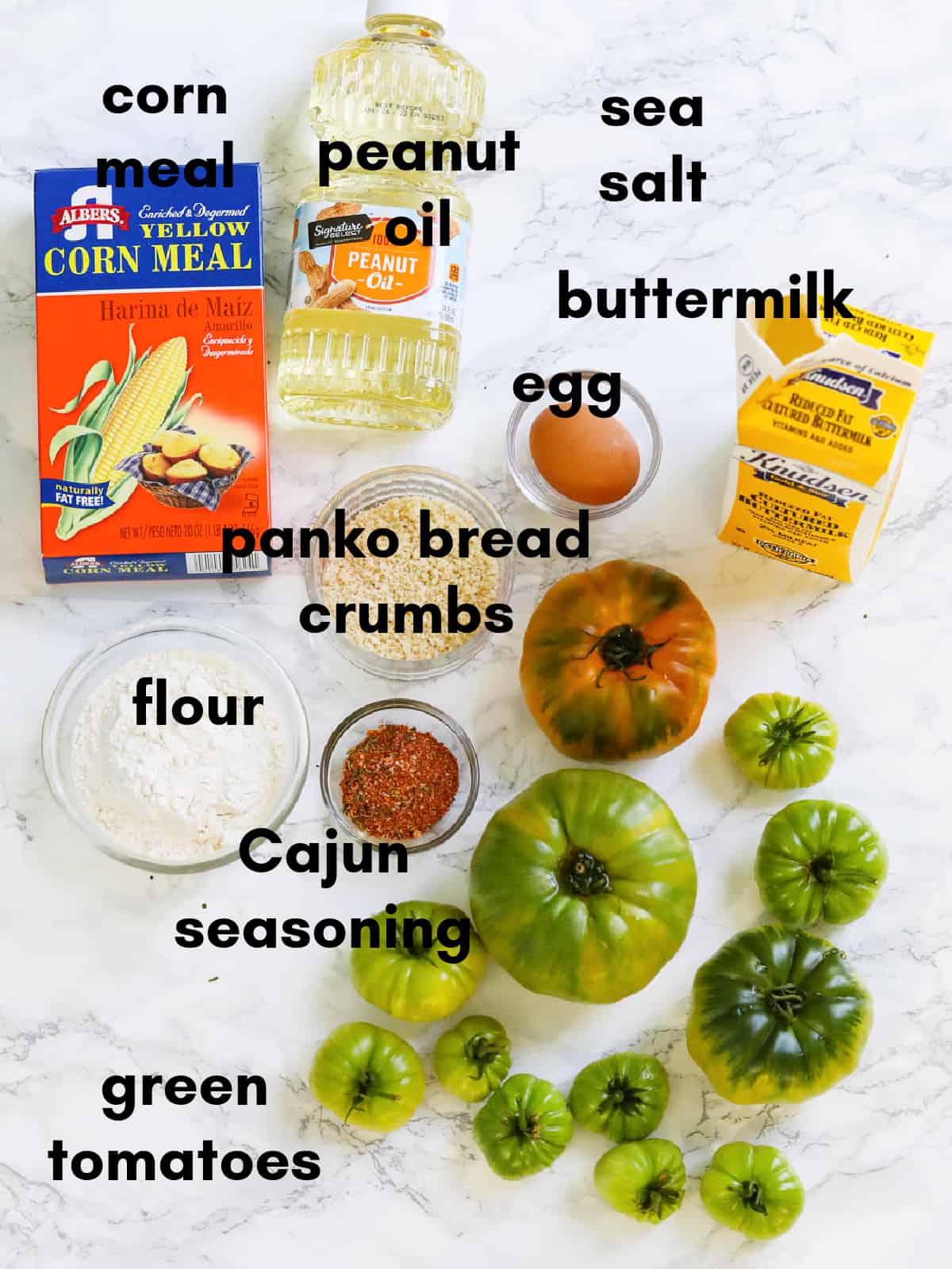 A white marble counter with ingredients including green tomatoes and bread crumbs to make fried green tomatoes.