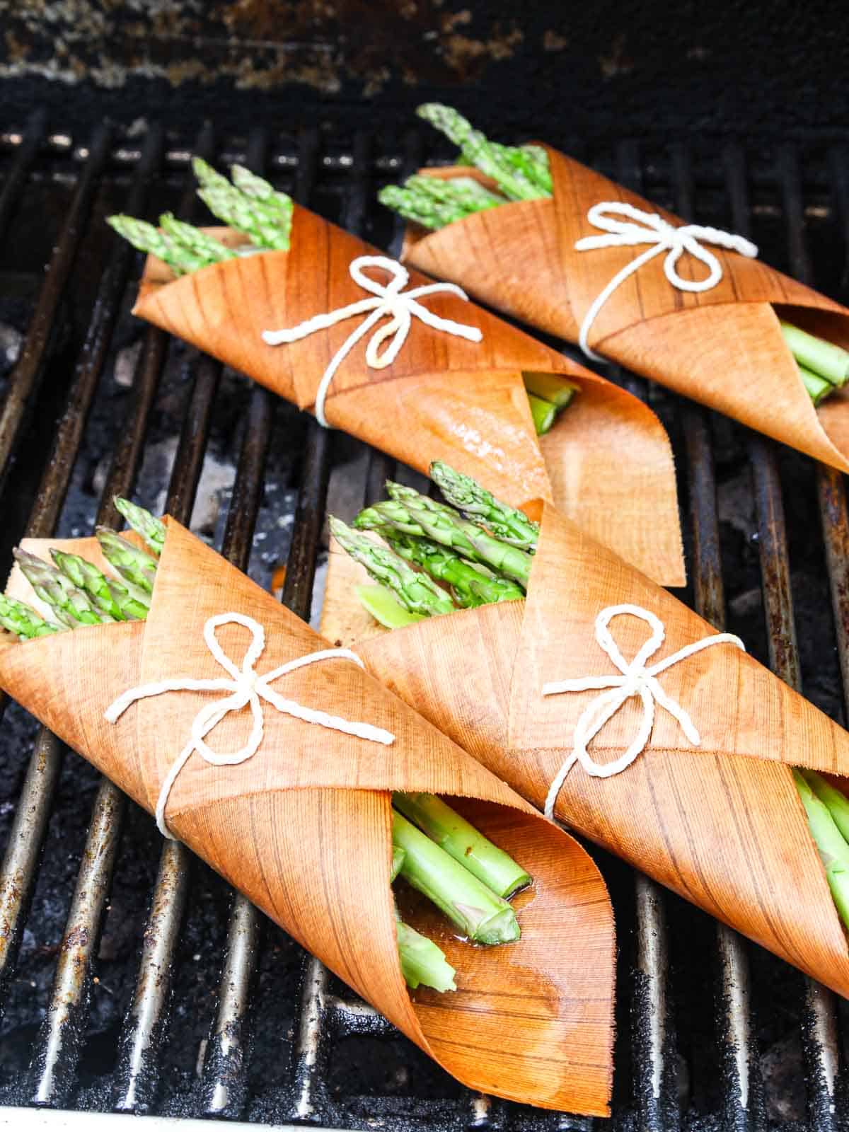 Cedar wrapped bundles of salmon and asparagus on the gas grill tied with kitchen string.