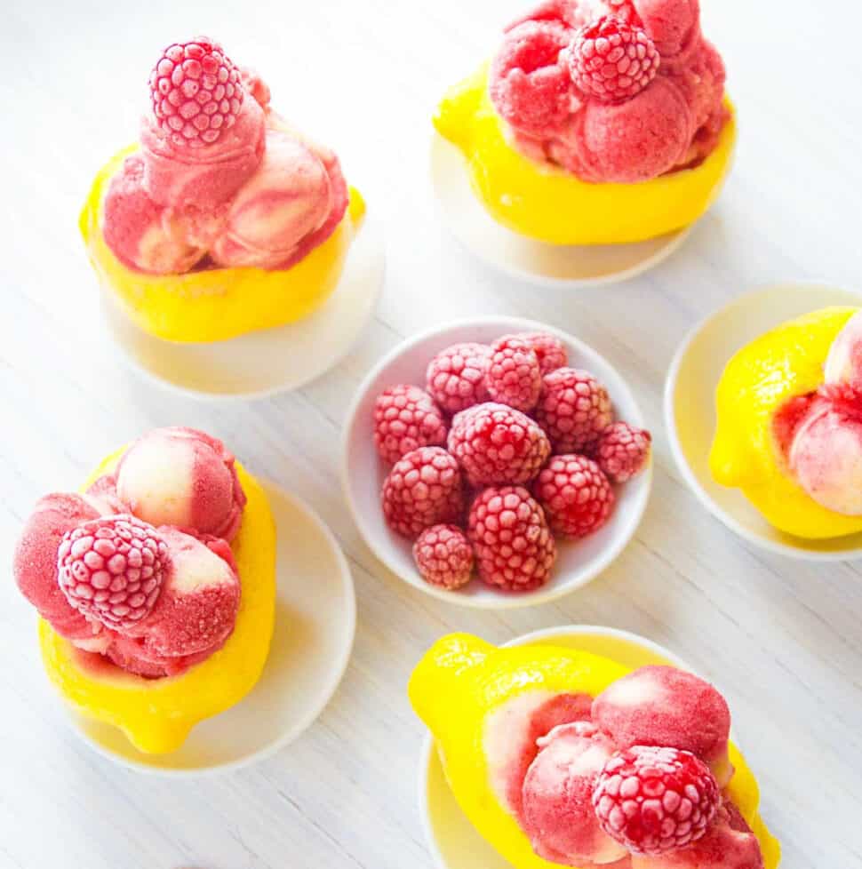 Bright yellow lemons carved out and filled with raspberry strawberry lemon sorbet as a summer dessert.