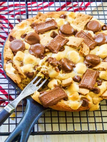 A cast iron skillet filled with a smore chocolate chip cookie with a fork inside.