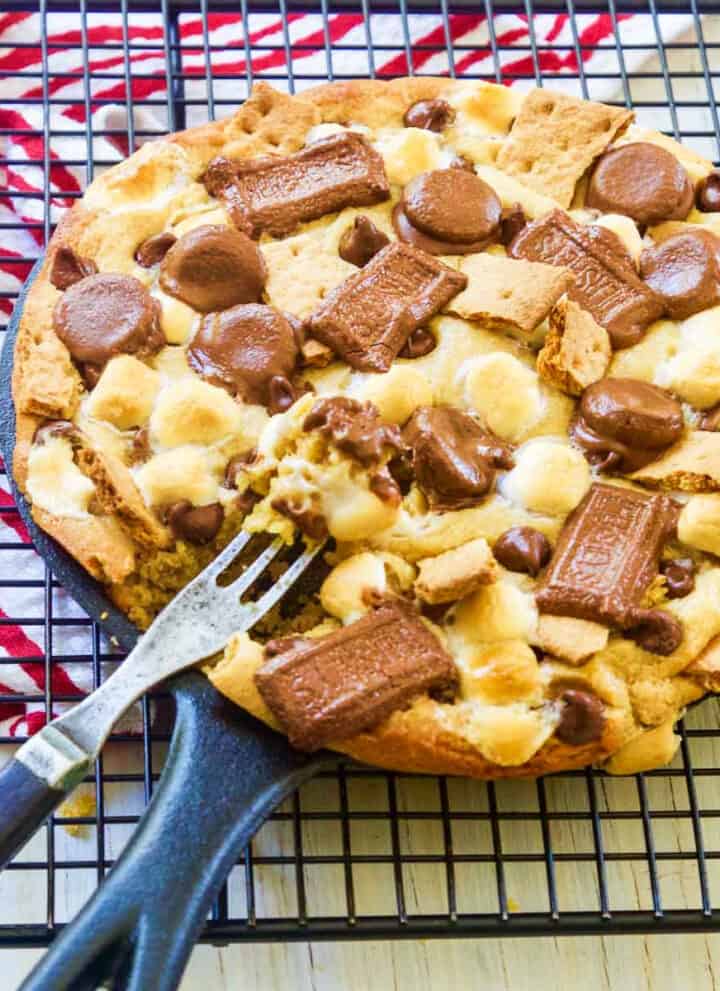 A cast iron skillet filled with a smore chocolate chip cookie with a fork inside.