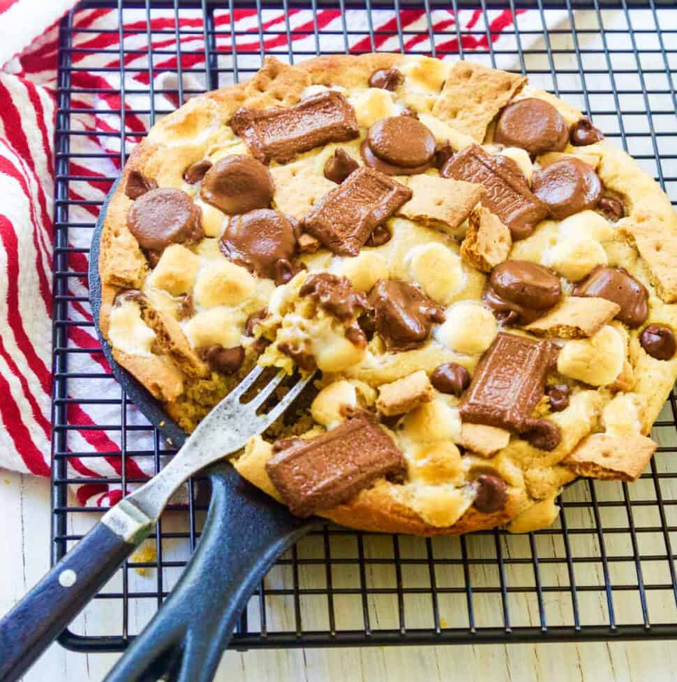 A cast iron skillet filled with a smore chocolate chip cookie with a fork inside.