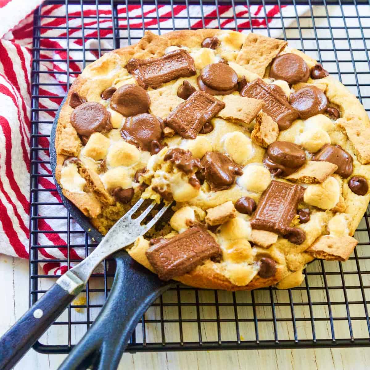 A cast iron skillet filled with a smore chocolate chip cookie with a fork inside.