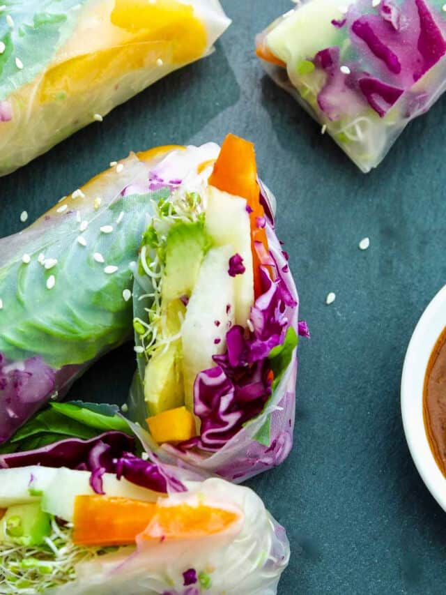 A vegetable spring roll or rice paper roll cut in half showing the bright veggies inside with a ginger dipping sauce in a small bowl.