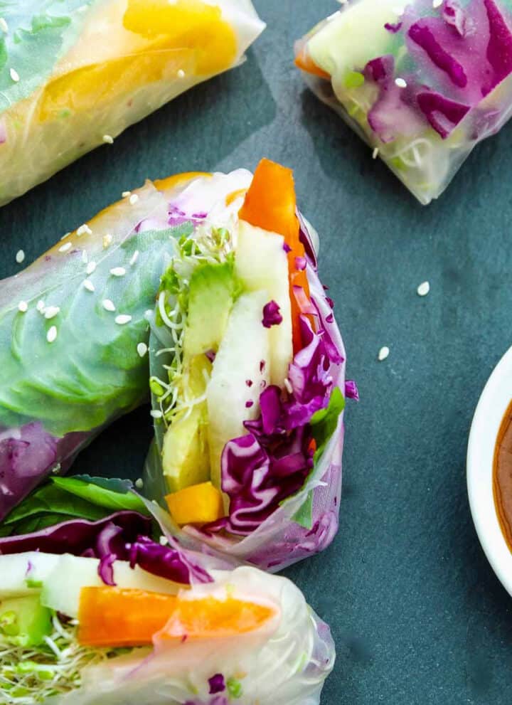 A vegetable spring roll or rice paper roll cut in half showing the bright veggies inside with a ginger dipping sauce in a small bowl.