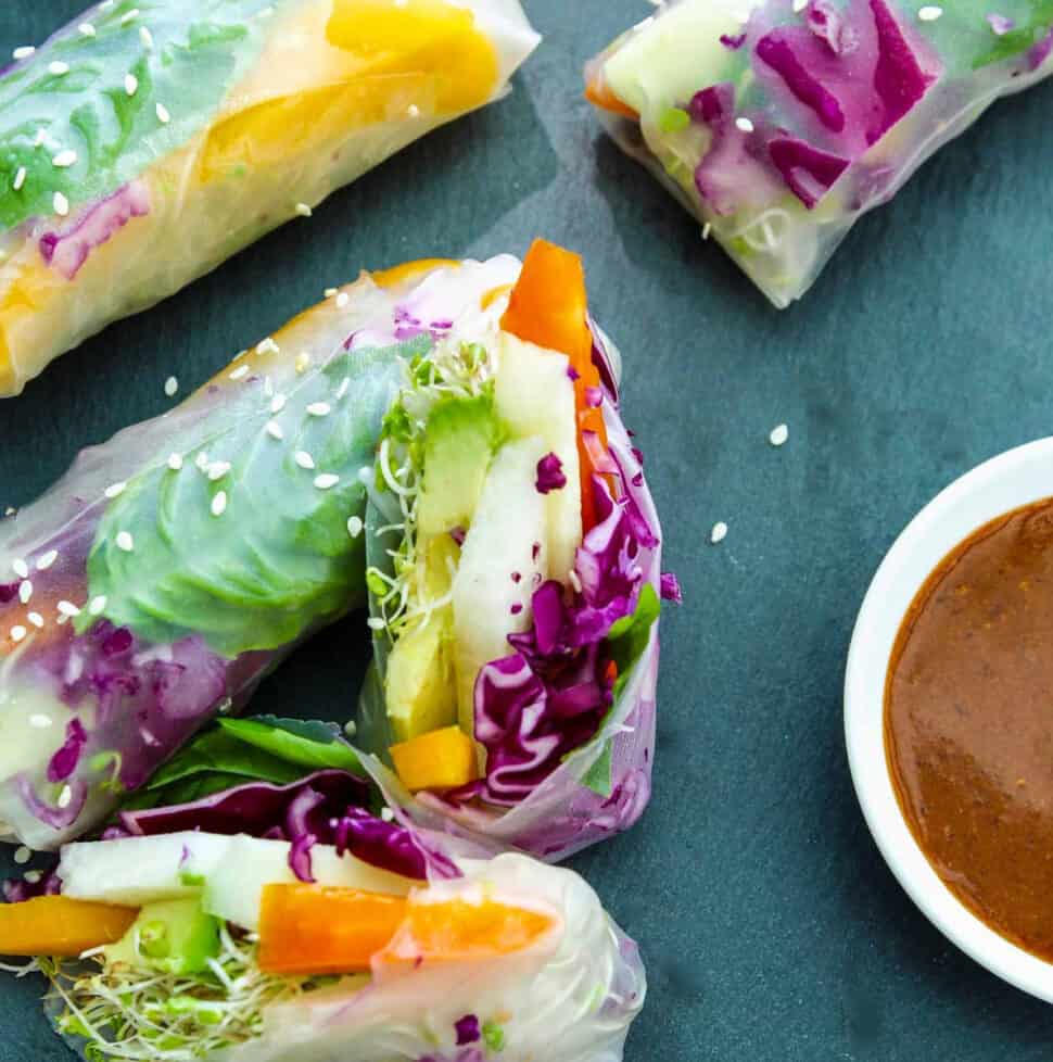 A vegetable spring roll or rice paper roll cut in half showing the bright veggies inside with a ginger dipping sauce in a small bowl.