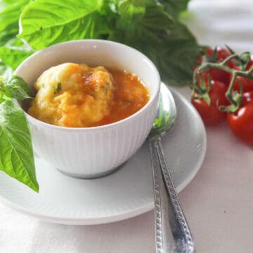 A bowl of tomato soup and cup of soup in a white cup garnished with fresh basil.