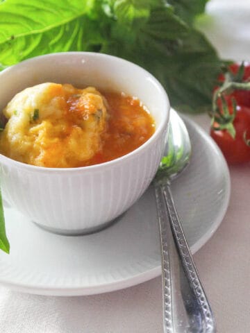 A bowl of tomato soup and cup of soup in a white cup garnished with fresh basil.