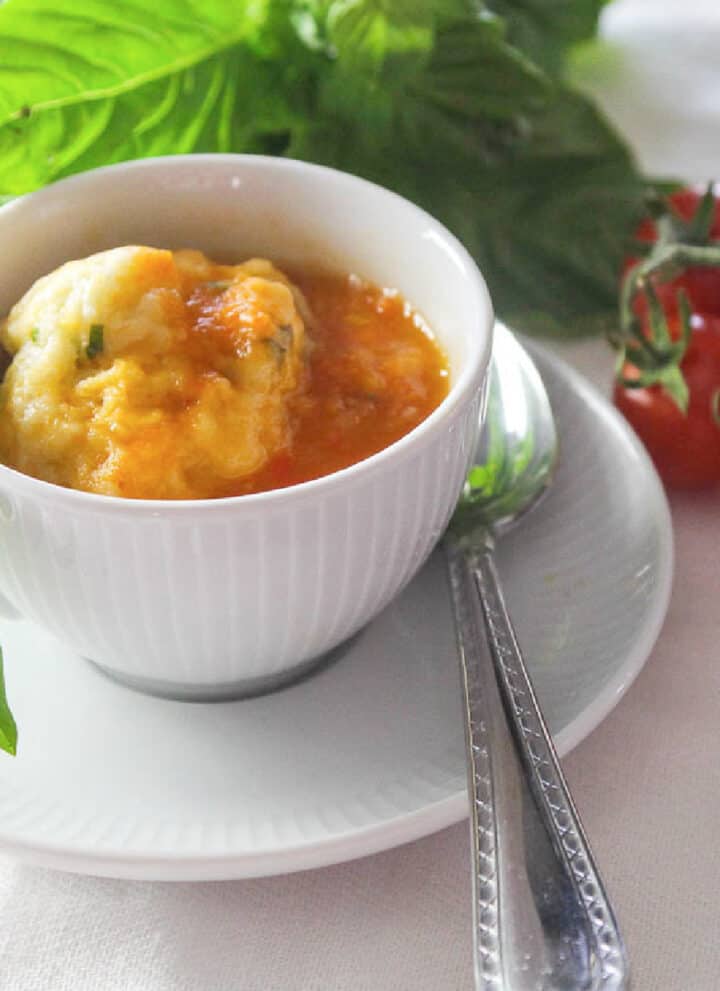 A bowl of tomato soup and cup of soup in a white cup garnished with fresh basil.