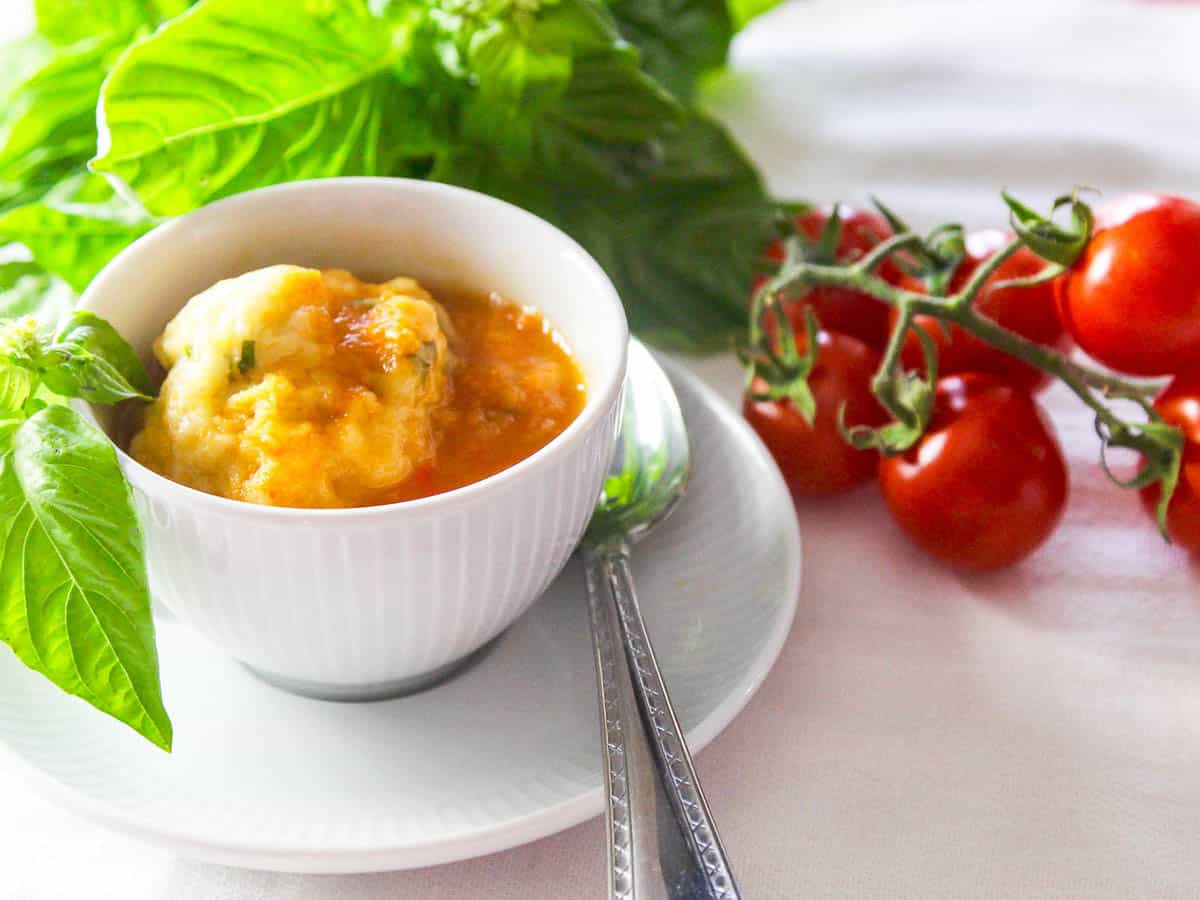 A white cup with tomato soup and basil dumplings.