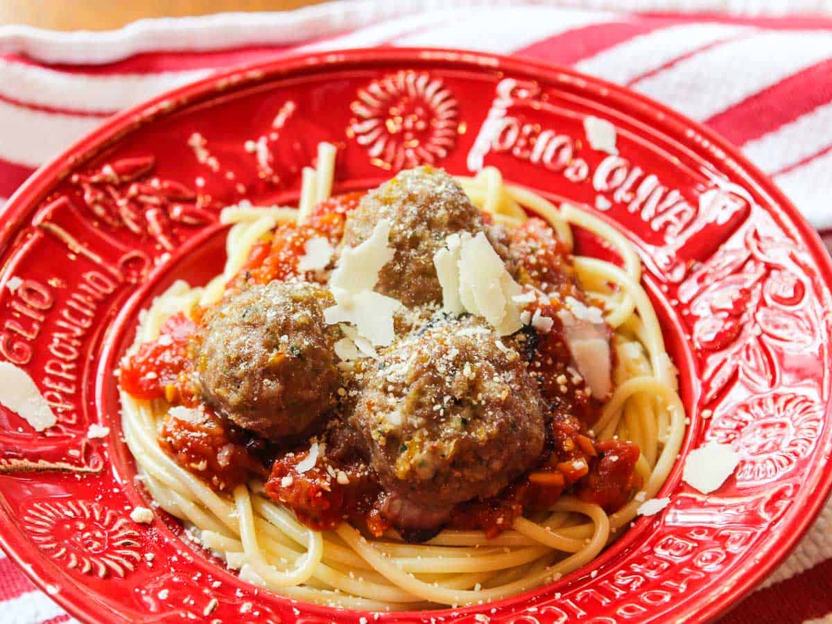 A red Italian bowl with hot pasta, sauce and turkey meatballs topped with shaved parmesan cheese.