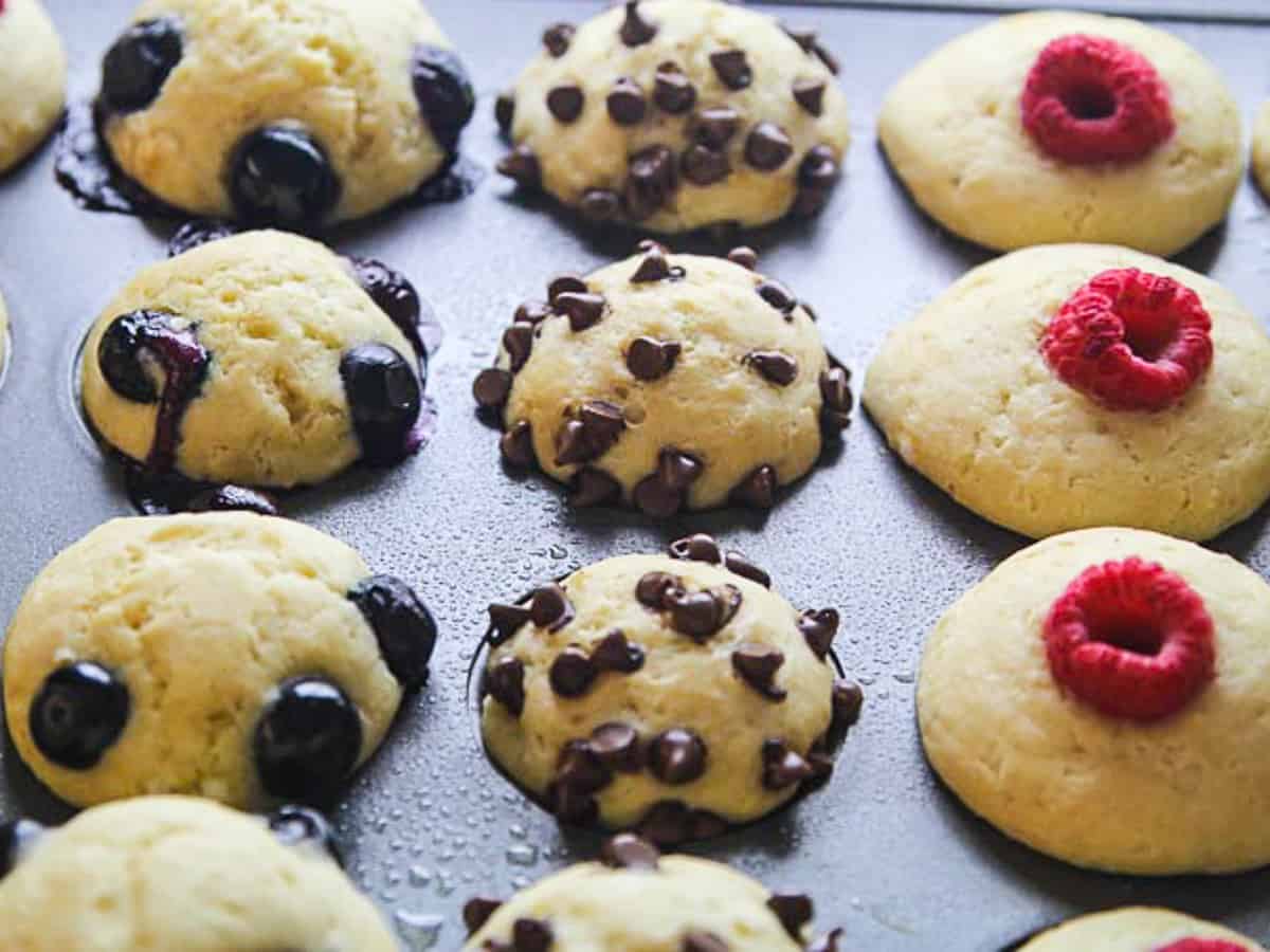 A full muffin pan filled with pancake muffins topped with blueberries, mini chocolate chips, and raspberries.