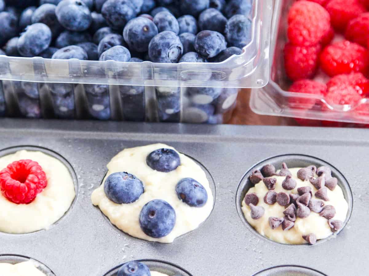 Pancake batter in a mini muffin tin with mini chocolate chips and berries.