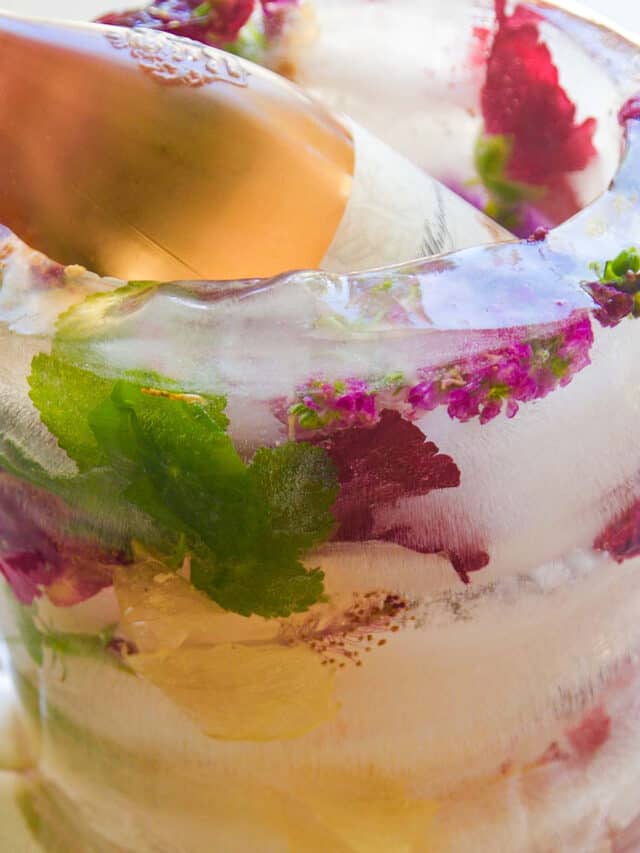 The side of a frozen floral ice bucket with pink and purple flowers and a bottle of wine inside chilling.