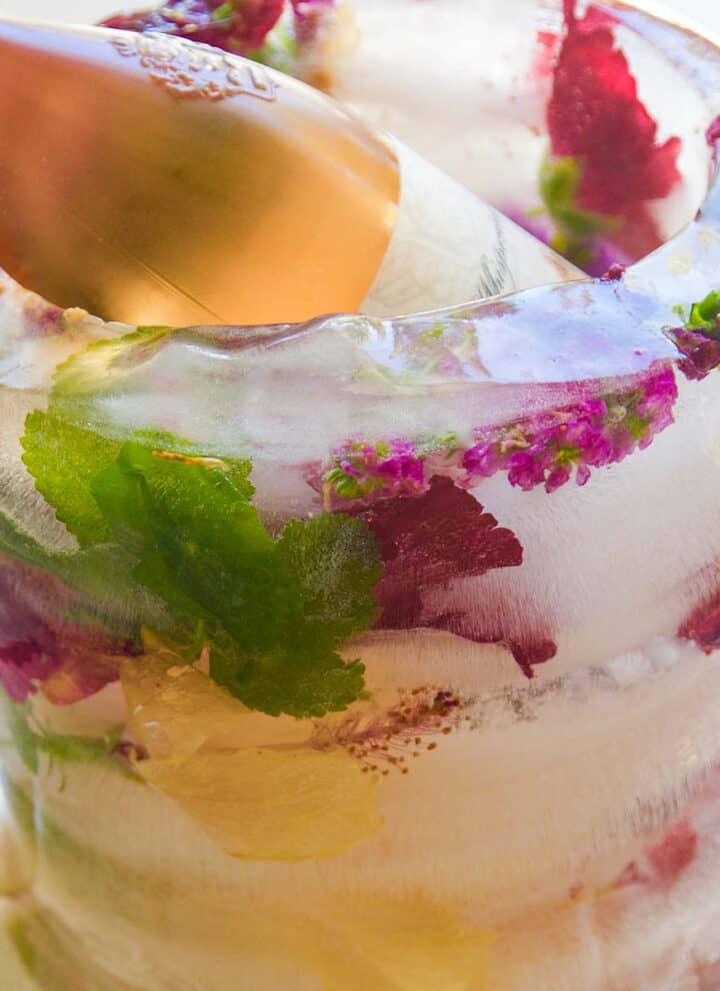 The side of a frozen floral ice bucket with pink and purple flowers and a bottle of wine inside chilling.