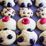 Baked pancake muffins in a tin topped with blueberries, mini chocolate chips, and raspberries.