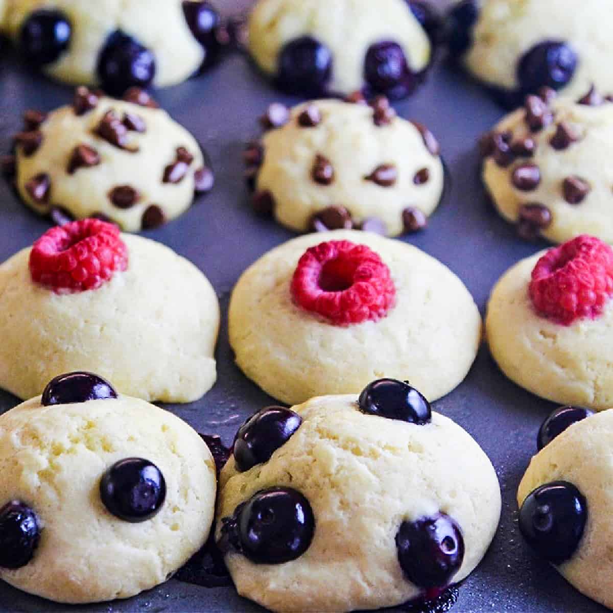 Baked pancake muffins in a tin topped with blueberries, mini chocolate chips, and raspberries.