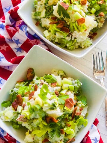 A small white bowl filled with bacon potato salad garnished with crispy bacon.