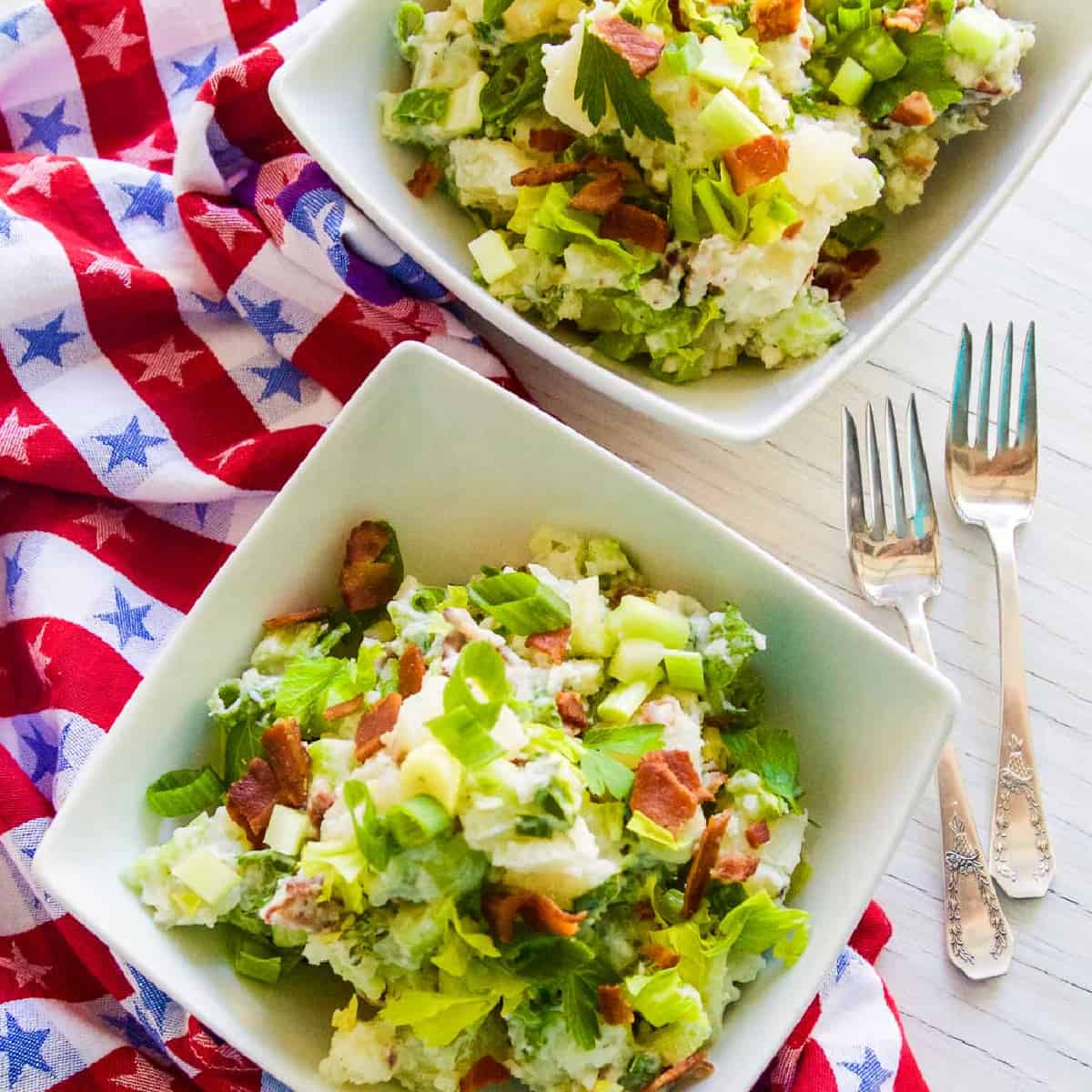 A small white bowl filled with bacon potato salad garnished with crispy bacon.