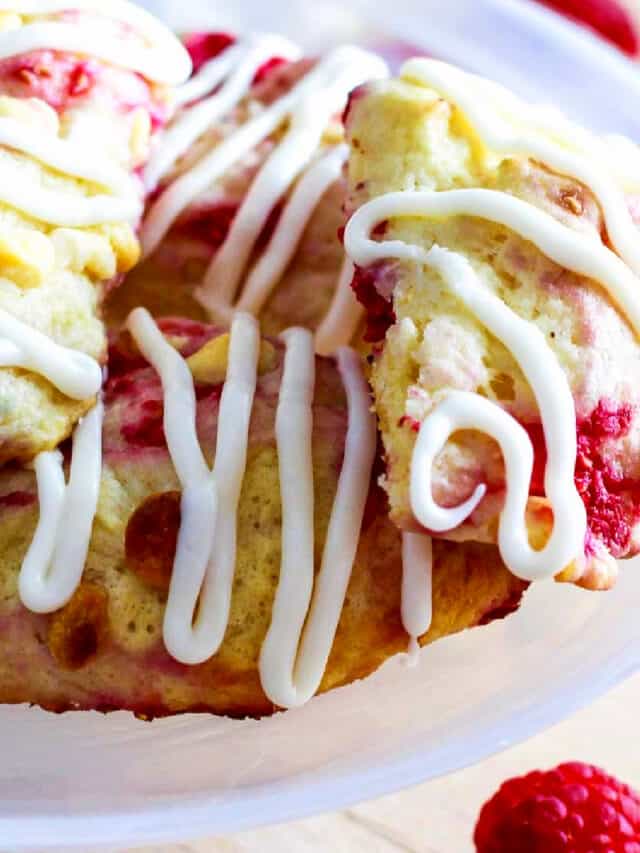 Small white cake plate with homemade raspberry scones studded with white chocolate chips and sweet red raspberries.