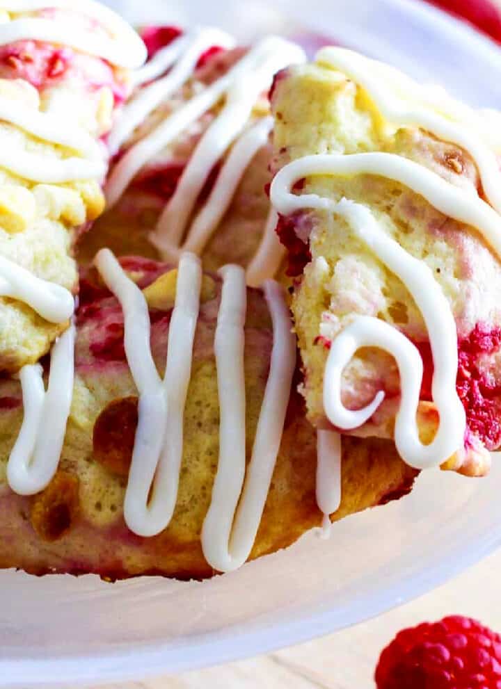 Small white cake plate with homemade raspberry scones studded with white chocolate chips and sweet red raspberries.