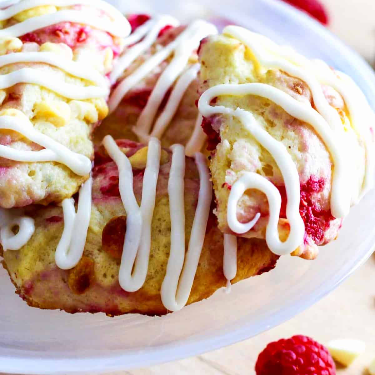 Small white cake plate with homemade raspberry scones studded with white chocolate chips and sweet red raspberries.